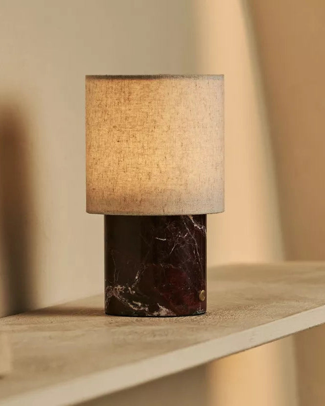 Table lamp with marble base and textured shade on a wooden shelf